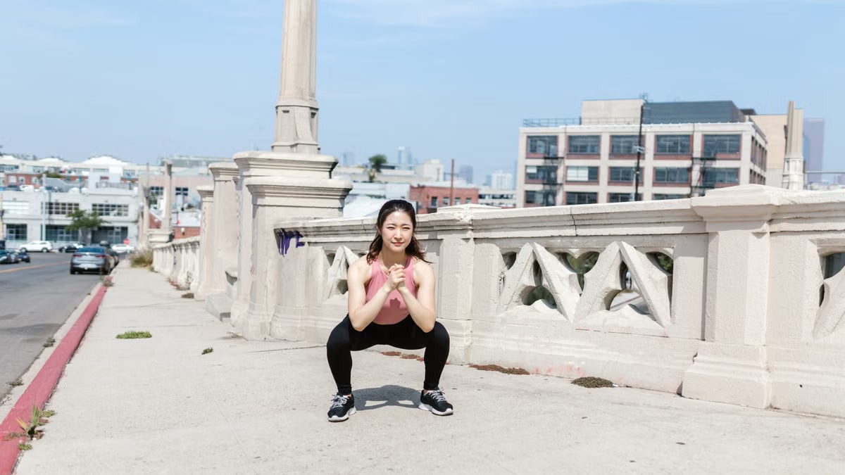 Woman exercising outdoors, performing squats on a city sidewalk.